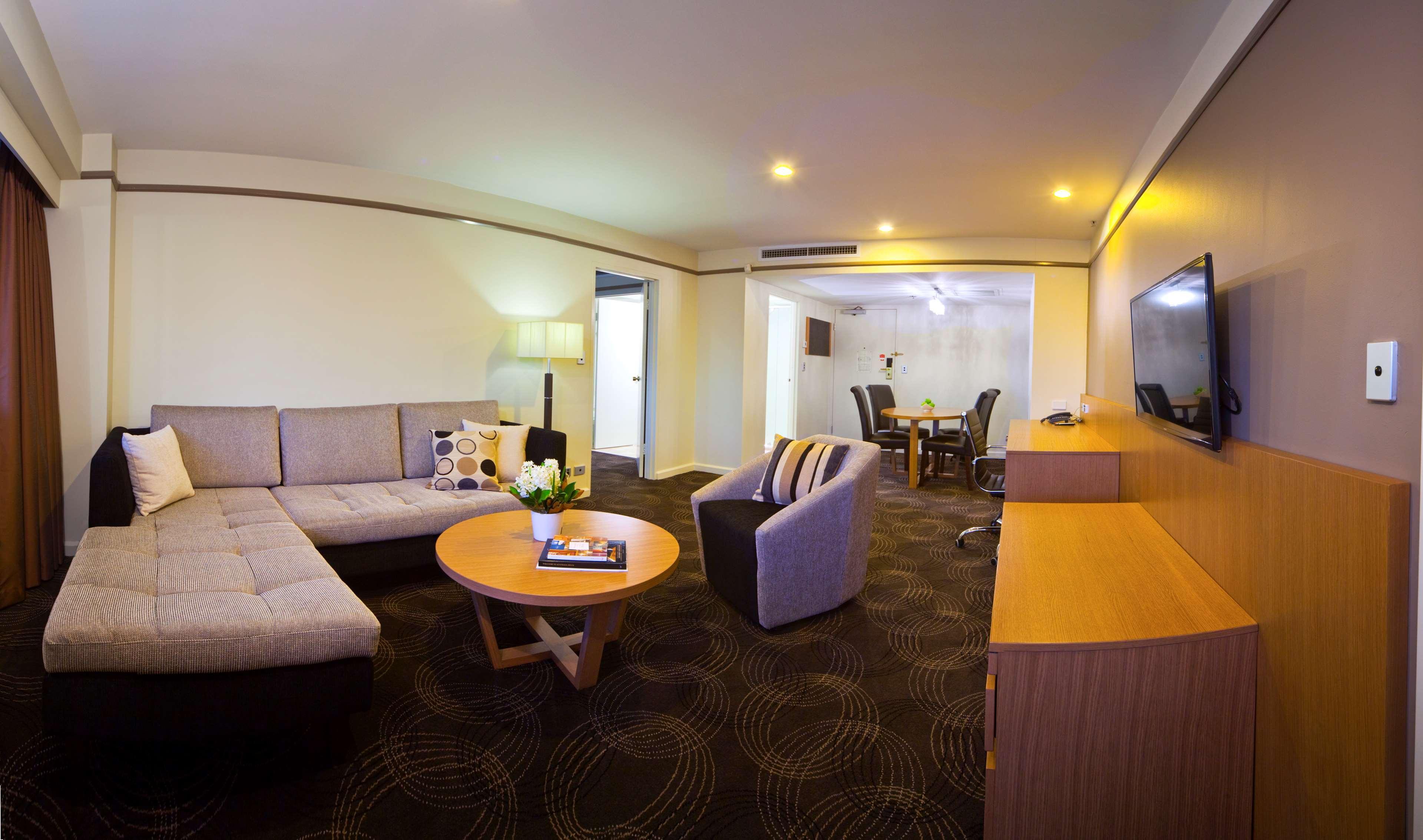 Hotel Stamford Plaza Adelaide Exterior foto The photo shows a spacious living area with modern decor. On the left, there is a light gray sectional sofa, accompanied by a round wooden coffee table in front of it. A couple of decorative pillows add a touch of color to the sofa. To the right, the