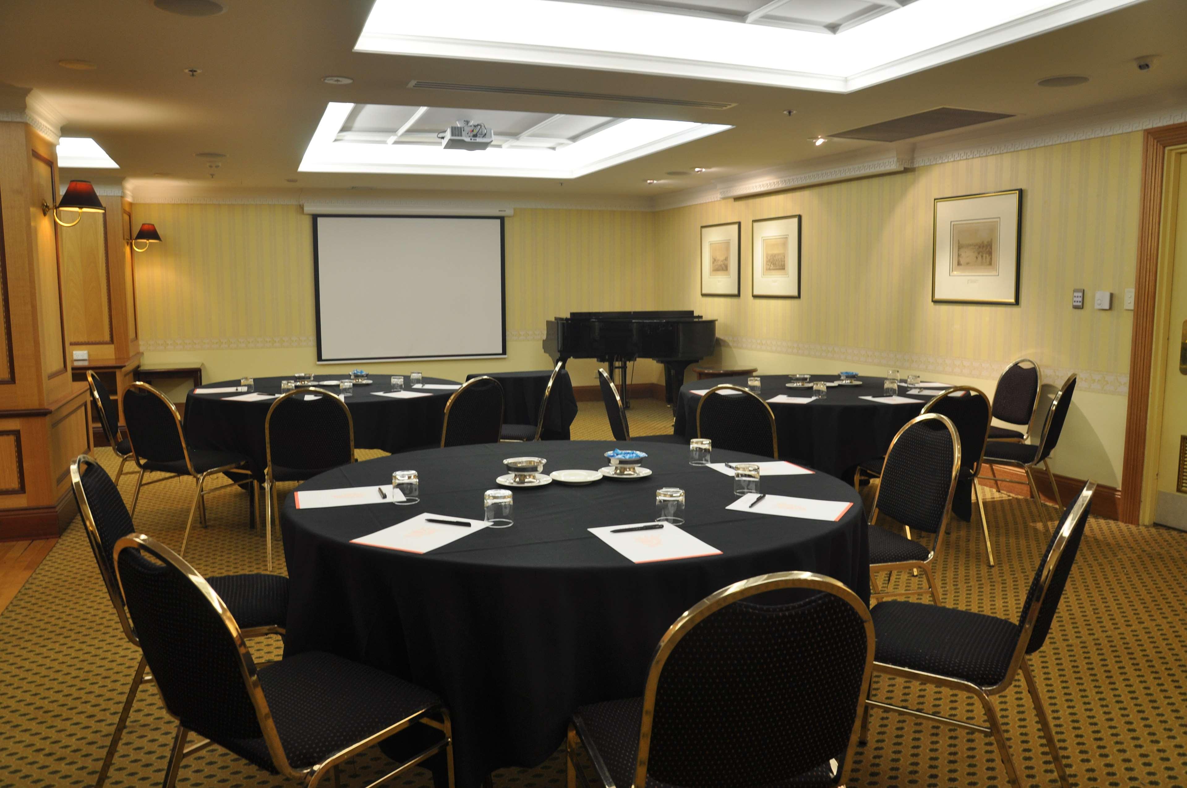 Hotel Stamford Plaza Adelaide Exterior foto The photo shows a conference room set up for a meeting or presentation. There are several round tables covered with black tablecloths, each surrounded by black upholstered chairs. On the tables, there are notepads and glasses of water, indicating tha