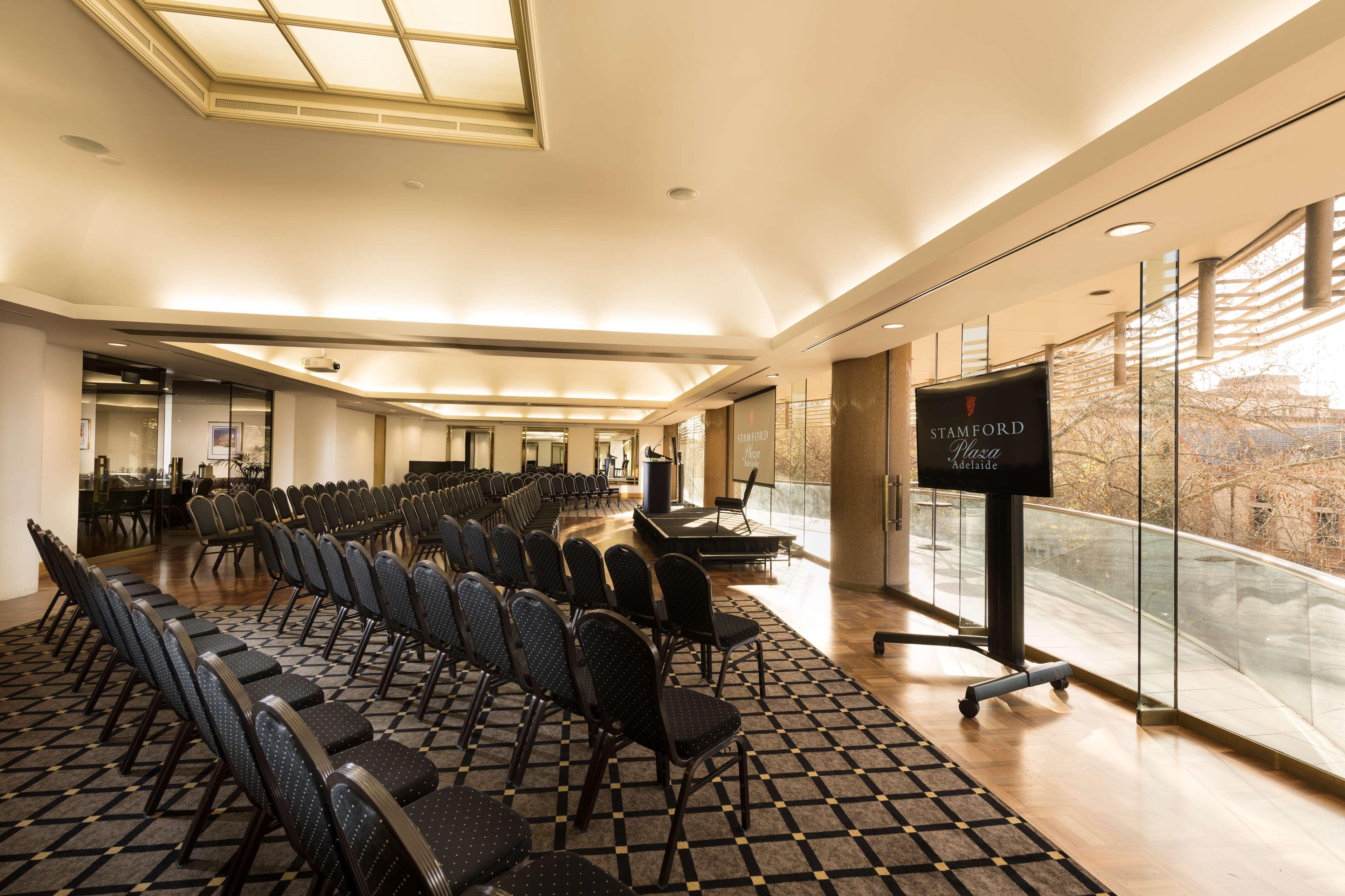 Hotel Stamford Plaza Adelaide Exterior foto The photo shows a large, elegantly designed event space or meeting room. There are rows of black chairs set up facing a presentation area. The flooring features a patterned carpet, and large windows allow natural light to enter the room. On one side,