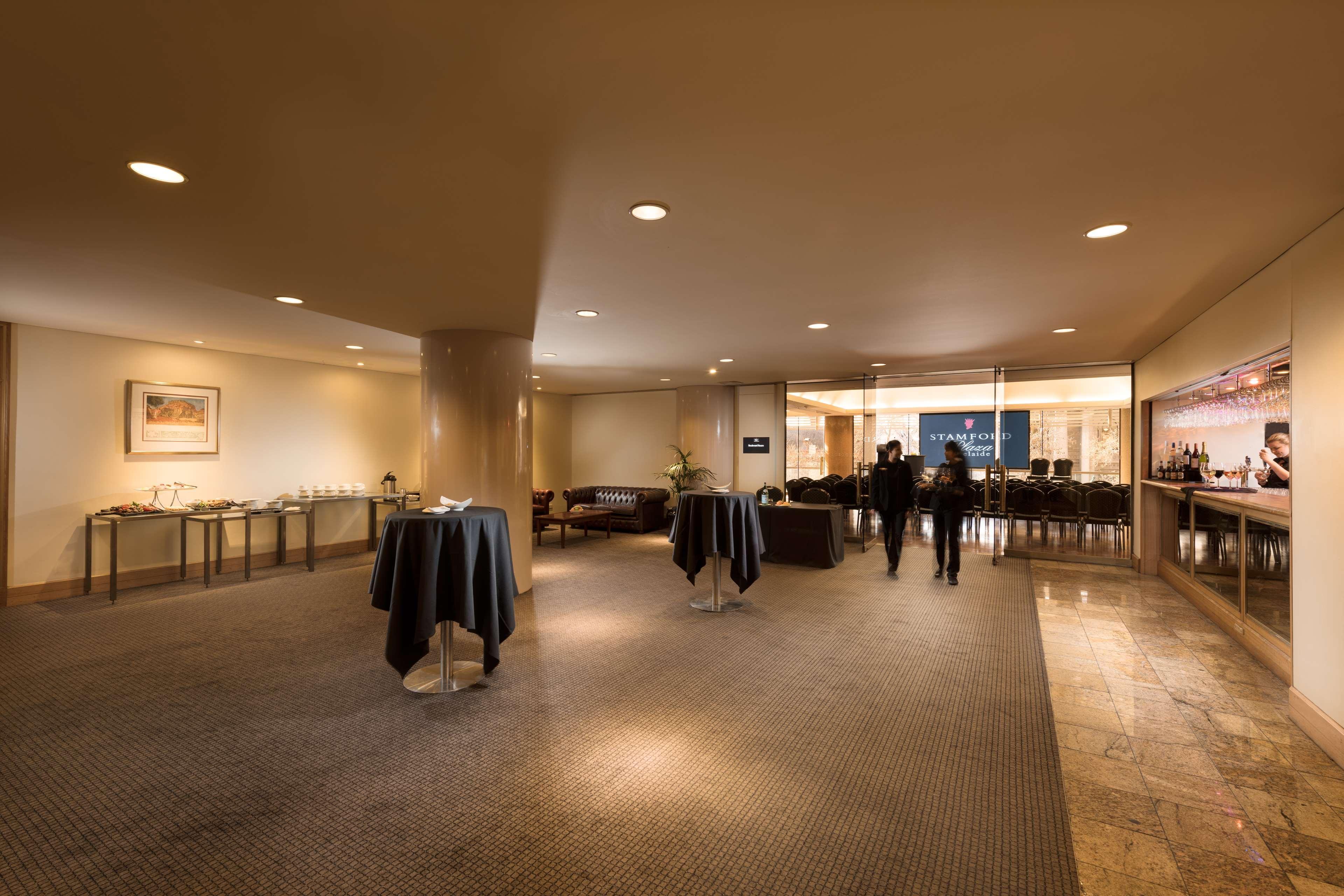 Hotel Stamford Plaza Adelaide Exterior foto The image shows an indoor space that appears to be a lounge or reception area. There are several round tables with dark tablecloths positioned throughout the room. The floor is carpeted, and the lighting is warm and somewhat dim. In the background, t
