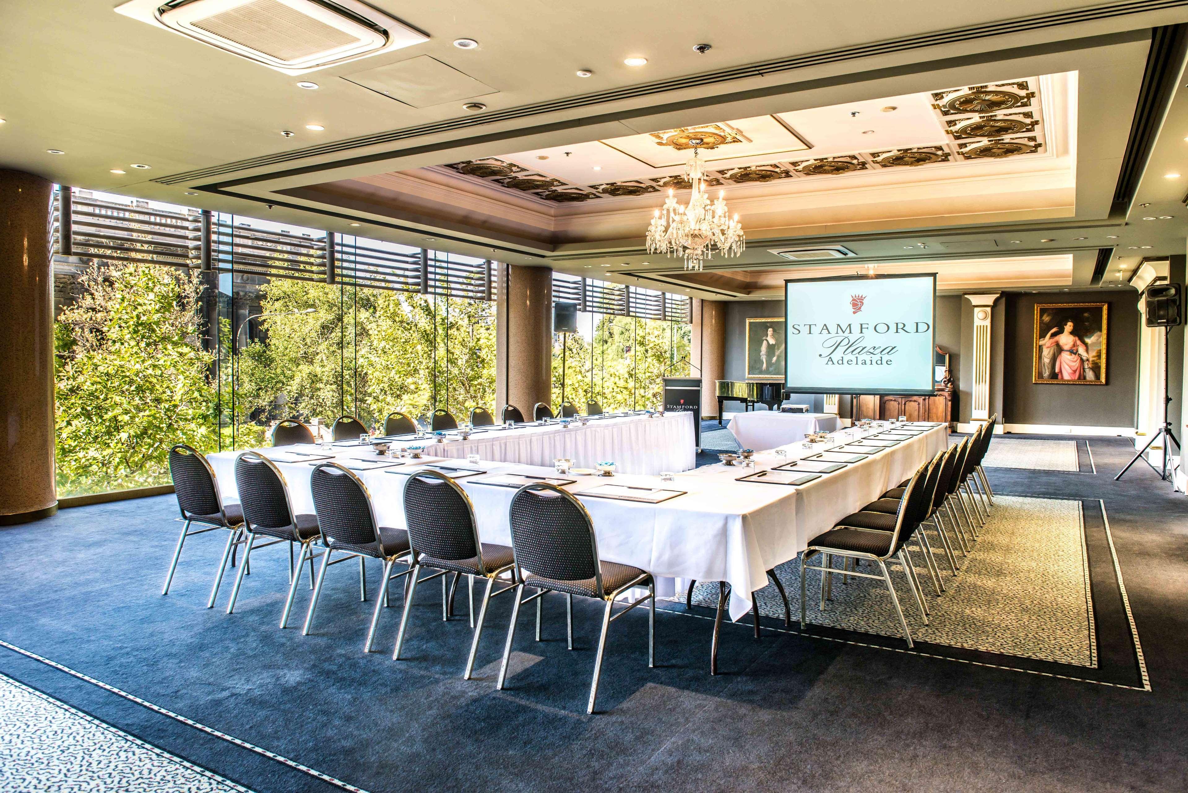 Hotel Stamford Plaza Adelaide Exterior foto The photo shows a stylish conference room set up for a meeting or event. There is a long rectangular table covered with a white tablecloth, surrounded by black chairs. A large screen displays the name "Stamford" along with a logo. The room features l