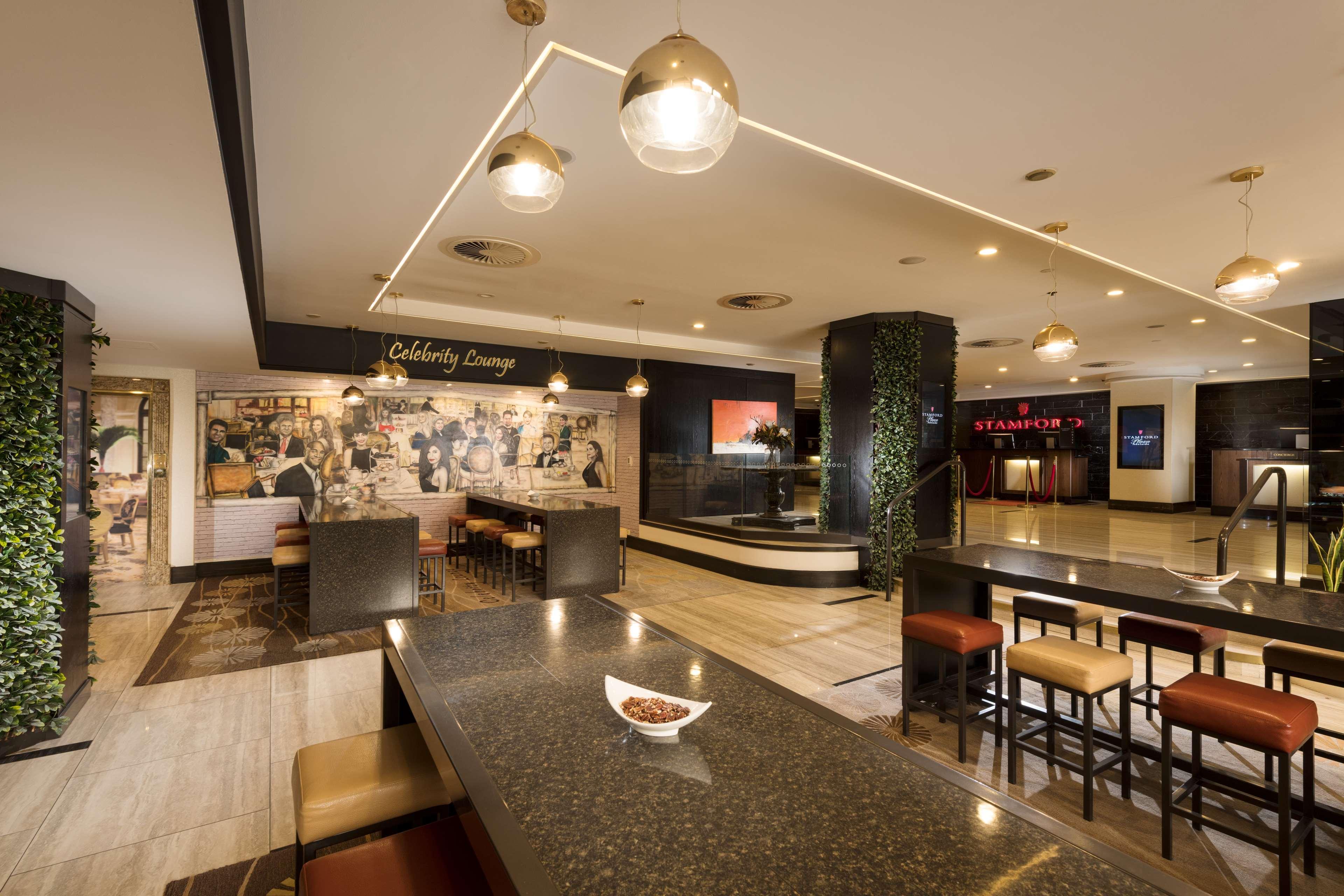 Hotel Stamford Plaza Adelaide Exterior foto The photo shows a modern and stylish interior of a lounge or restaurant area. Prominent features include a long dark countertop with bar stools, and several pendant lights hanging from the ceiling. In the background, there is a mural or artwork that 
