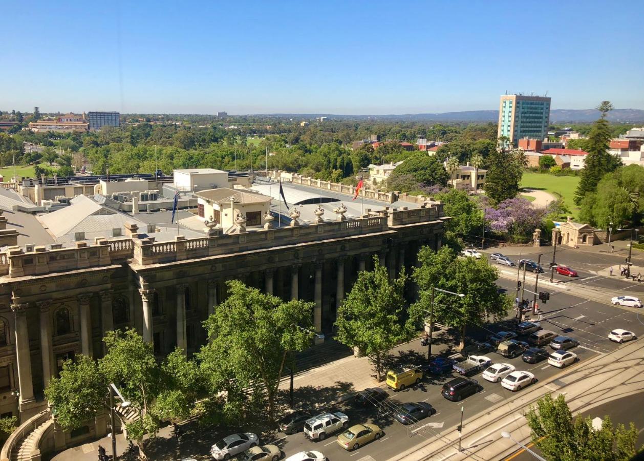 Hotel Stamford Plaza Adelaide Exterior foto The photo depicts a cityscape view, showcasing a mix of architectural structures and greenery. In the foreground, there is a large, classical building with columns, suggesting it may be a historical or governmental structure. Surrounding the building